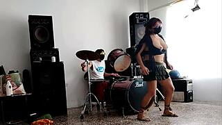 They play the drums for her. She dances stripping and showing her ass.